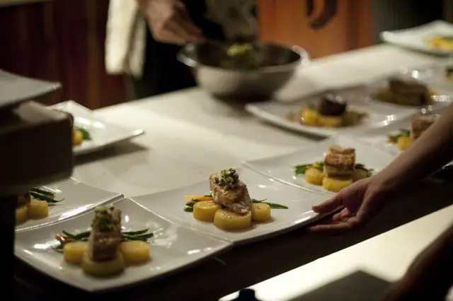 A row of plates being finished on the pass — fish over potato with green beans and herb salsa